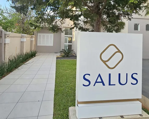 Entrada da Clínica Salus: o totem branco com o nome SALUS na frente do terreno e o caminho de piso claro que leva até a porta