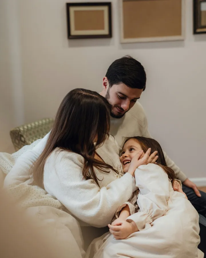 Pai, mãe e a filha pequena abraçados no sofá de casa