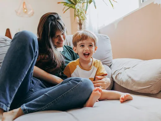Mãe e filho pequeno rindo juntos no sofá